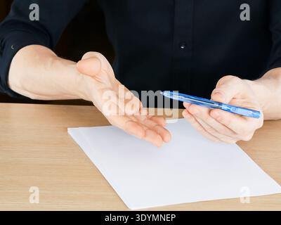 Person poised to write with ballpoint pen over white sheet on table surface Stock Photo