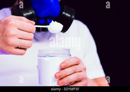 Dramatic shot of hands in gas mask environment adding powdered material to jar on dark setting. Stock Photo