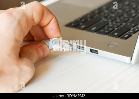 Hand holding a white USB 2.0 to Fast Ethernet Adapter with attached USB cable on a light wooden table, a compact tool for adding wired networking to d Stock Photo
