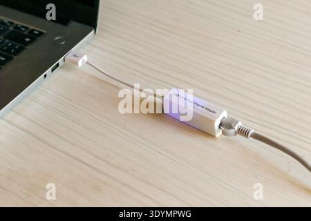 White USB to Ethernet network adapter plugged into a laptop port, with short white cable and RJ45 connector Stock Photo