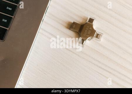 A compact multi-port USB drive connected to the edge of a silver laptop resting on a white wooden desk, facilitating quick and efficient data operatio Stock Photo