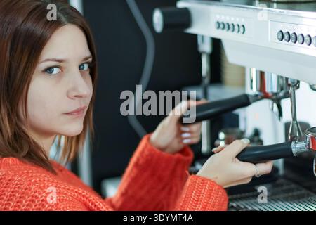 Barista in vibrant orange knit sweater operating professional coffee equipment in cafe workspace Stock Photo