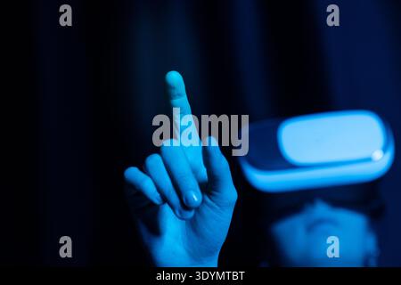 Young woman wearing virtual reality headset and pointing forward while interacting with a virtual interface Stock Photo