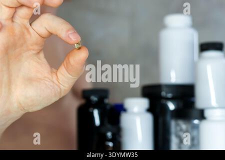 Man presenting small capsule against supplement jars. Athletic man holding up a nutritional capsule with assortment of dietary supplement containers i Stock Photo