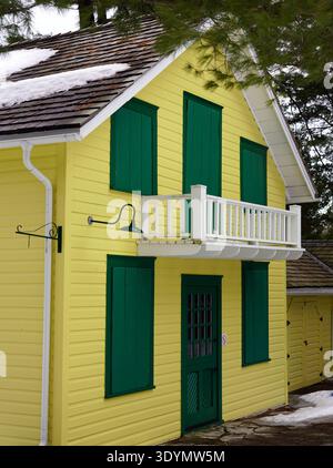A vibrant yellow two-story house features a white balcony and dark green shutters on all windows and the front door Stock Photo