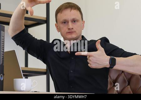 Adult male in black attire seated with laptop and mug, using framing and pointing gestures in contemporary professional space. Stock Photo