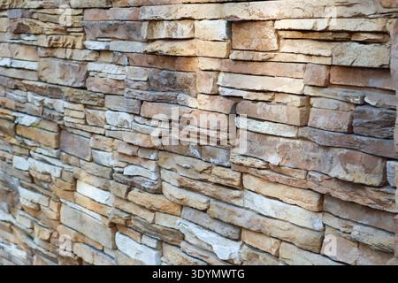 Close-up of warm beige natural stone cladding with varied brick sizes and subtle color variations on an exterior wall. Stock Photo