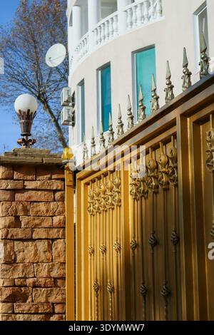 Classic bronze lantern with white frosted shade on brick pedestal next to ornate columned facade, featuring surveillance dome under clear sky. Stock Photo