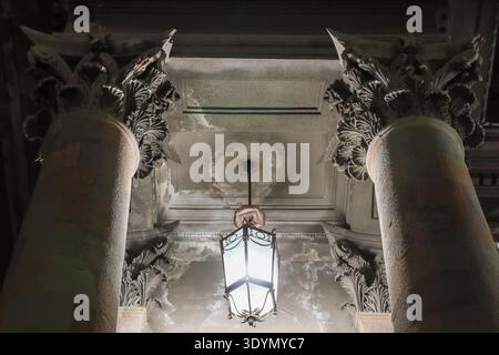 Detailed view of ornate Corinthian capitals and hanging lantern on aged ceiling with peeling paint in classical interior Stock Photo