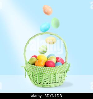 Color Easter eggs falling into basket on light blue gradient background Stock Photo