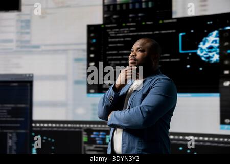 African american software engineer immersed in code development, studying programming language for innovation and data science. Coding life with digital interfaces and terminal window. Stock Photo