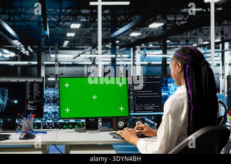 Admin in data center managing AI training datasets using green screen PC. Woman using chroma key PC to oversee machine learning in server room supporting scalable infrastructure for AI apps Stock Photo