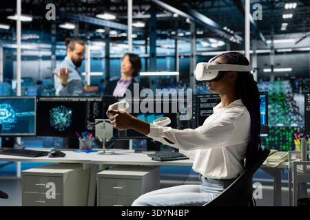 Server farm worker using virtual reality tech, deploying deep learning tools to automate repetitive workflows. Data center technician wearing VR headset managing datasets used in AI training Stock Photo