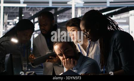 System administration team collaborating on AI automation deployment in data center. Server farm staff members adjusting machine learning configurations, working together, camera A Stock Photo