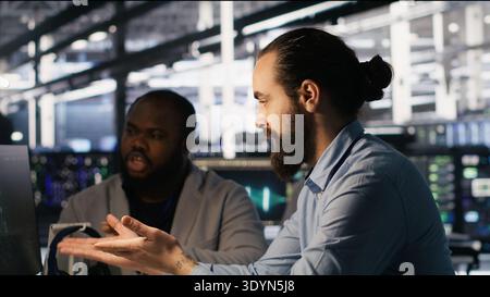 Lead data center engineer oversees team integrating AI automation tools during infrastructure maintenance. Worker under manager supervision uses machine learning models for operational tasks, camera A Stock Photo
