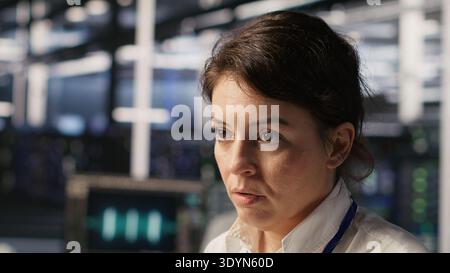 Tired data center engineer stretching, monitoring server clusters performing AI training. Fatigued server farm IT specialist supervising computing systems managing deep learning operations, camera A Stock Photo