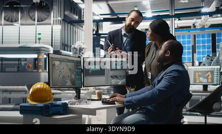 Multiethnic team of experts collaborating in a solar panel power plant, reviewing blueprints and production line metrics to ensure clean energy manufacturing and sustainability. Camera A. Stock Photo