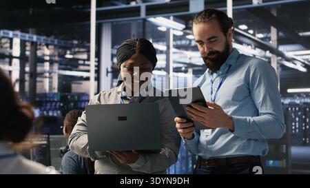 Data scientists working together in server room, reviewing neural network code and LLM visualization dashboards. Team of IT experts coordinating tasks, monitoring AI system performance, camera A Stock Photo