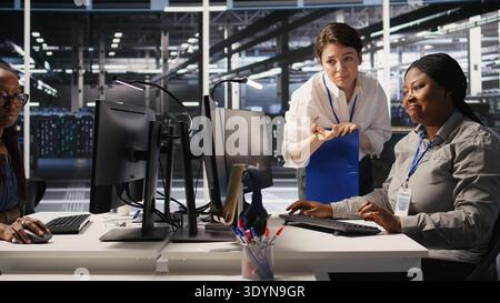 Happy data center manager pleased by work done by team integrating AI automation tools in infrastructure maintenance. Smiling supervisor satisfied by worker upgrading machine learning models, camera A Stock Photo