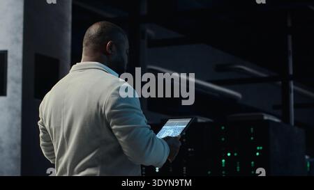 Software developer in data center using tablet, employing AI machine learning models. Employee using device to fulfill artificial intelligence infrastructure needs, allocating resources, camera B Stock Photo