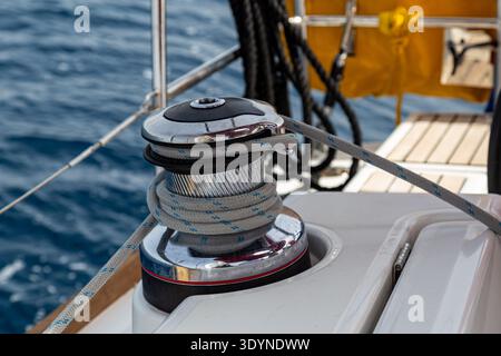 A close-up view of a sailing winch with a rope wrapped around the metallic drum on the deck of a yacht. The image shows detailed nautical equipment Stock Photo