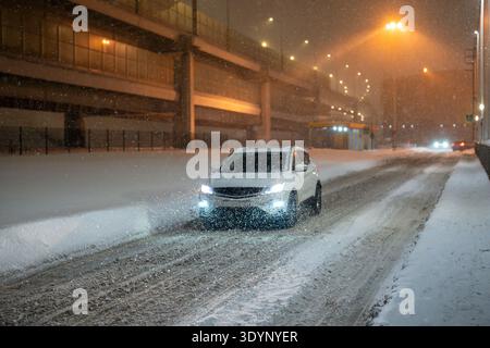 Heavy snowfall and blizzard in city, car driving through roads covered with snow and ice. Stock Photo