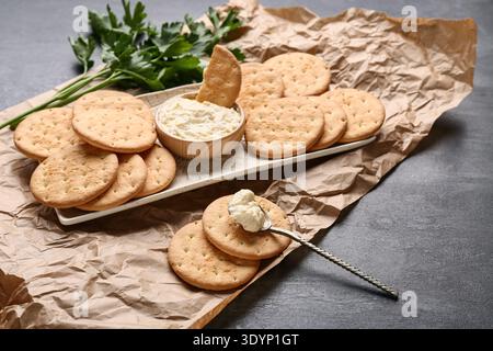 Tasty crackers with bowl of sauce and parsley on black grunge background Stock Photo