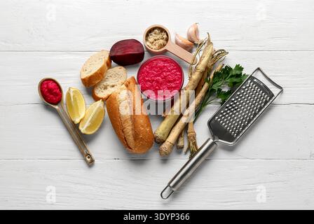 Bowl of horseradish sauce with beet, ingredients and grater on white wooden background Stock Photo