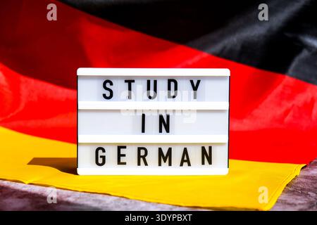 Lightbox with text STUDY IN GERMAN National symbol of Germany. German wave silky flag background. Concept of education and learning  Stock Photo