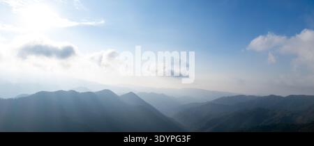 Rolling mountain peaks and valleys in the early morning light. Sunlight breaking through clouds, casting rays on the landscape. Blue sky, freedom, bri Stock Photo