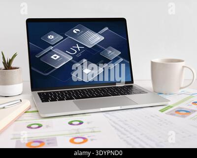 Laptop showing UX design, user interface, and digital marketing concepts. Coffee cup, plant, and financial charts on desk Stock Photo