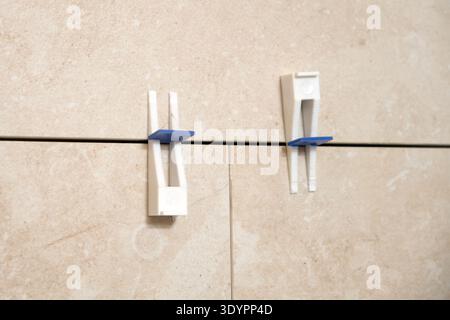 Close-up of porcelain wall tiles with plastic leveling clips keeping grout lines even during bathroom renovation and tile installation process. Stock Photo