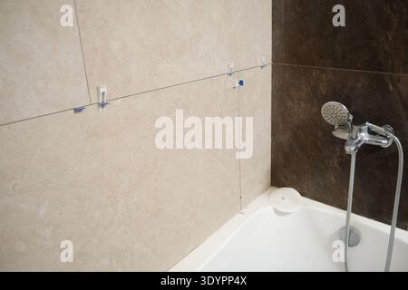 Bathroom renovation with newly installed porcelain stoneware wall tiles above bathtub, using spacers and leveling clips before grouting. Stock Photo