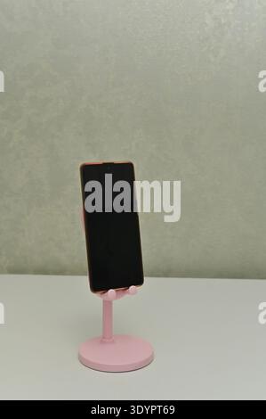 Smartphone mounted on stand shown closeup, smart phone screen facing forward, smartphone fixed on pink holder, isolated background, modern technology Stock Photo