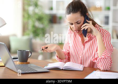 Confused self employed talking on phone and checking paper agenda working at home Stock Photo