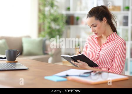 Serious freelance worker taking notes in paper agenda working at home Stock Photo