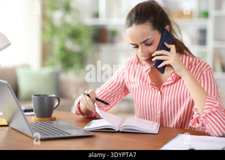 Pensive freelance worker talking on phone checking agenda working at home Stock Photo