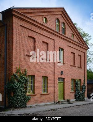 Historic red brick building facade with green windows and entrance door in a quiet urban street with traditional architecture and brick texture. Stock Photo
