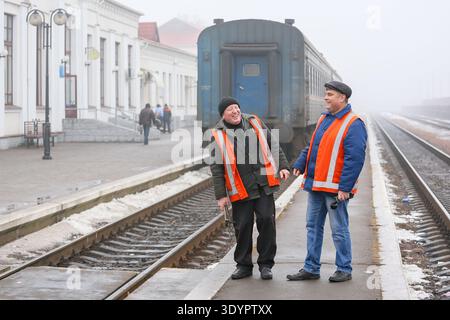 January 19, 2015, Romny, Ukraine: Two railway workers in orange protective vests are chatting on a foggy platform near an old blue train Stock Photo