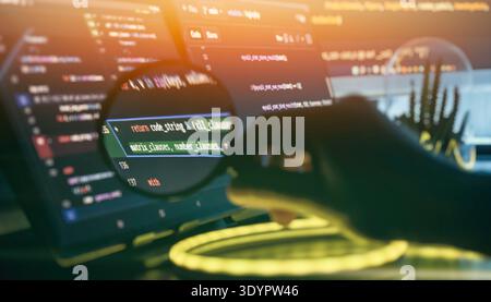 Magnifying Glass Inspecting Source Code on Tablet and Monitor with Neon Light in Developer Stock Photo