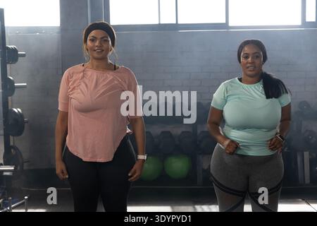 African American women standing and jogging together in gym near dumbbell rack and medicine balls Stock Photo