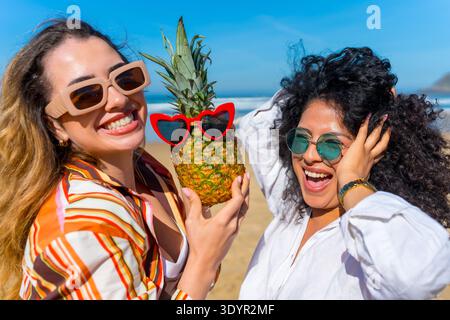 Two young friends having fun with pineapple on beach Stock Photo