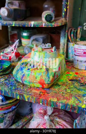 Close-up of a paint mixing machine completely covered with layers of colorful paint splashes in an art studio, surrounded by jars, cans and tools on a Stock Photo