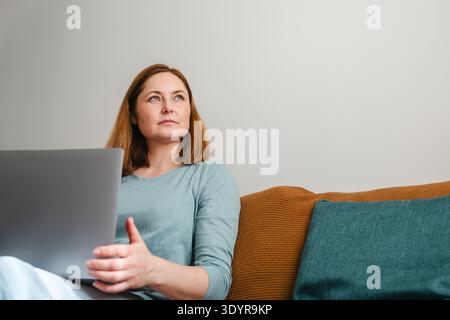 Woman sitting on sofa with laptop, work from home, copy space Stock Photo