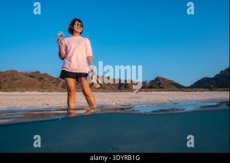 woman enjoying a glass of wine on a beach in Komodo national park Stock Photo