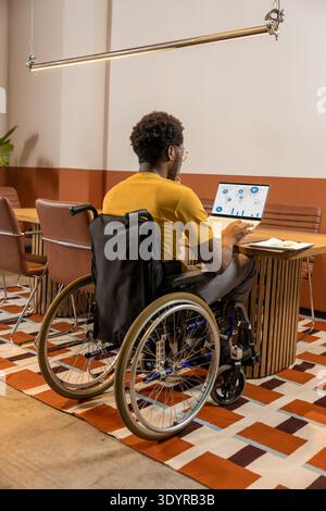 Man in wheelchair working attentively on laptop with migration analytics Stock Photo