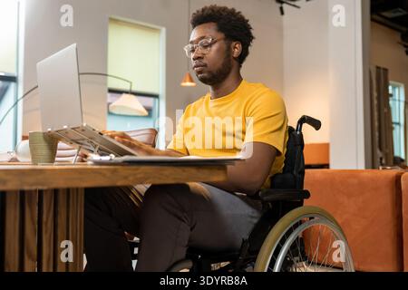 Man in wheelchair working on laptop with online business data in coworking space Stock Photo