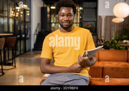 Confident man resting on couch with notepad smiling in coworking environment Stock Photo