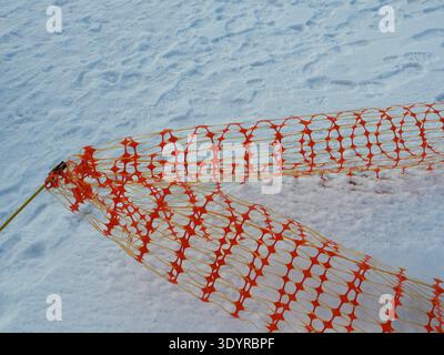 Orange plastic safety fence on snow with strong color contrast and graphic net pattern. Copyspace Stock Photo
