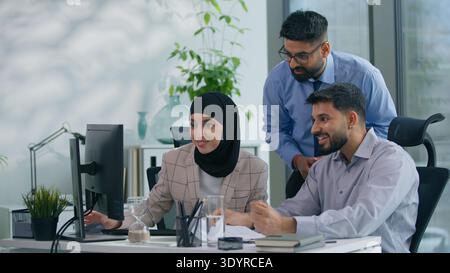 Excited smiling happy Arabian Muslim business team in office looking at computer online work job with pc internet teamwork motivation career Stock Photo